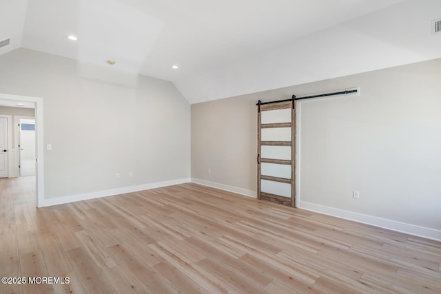 unfurnished room with light wood-type flooring, a barn door, and vaulted ceiling