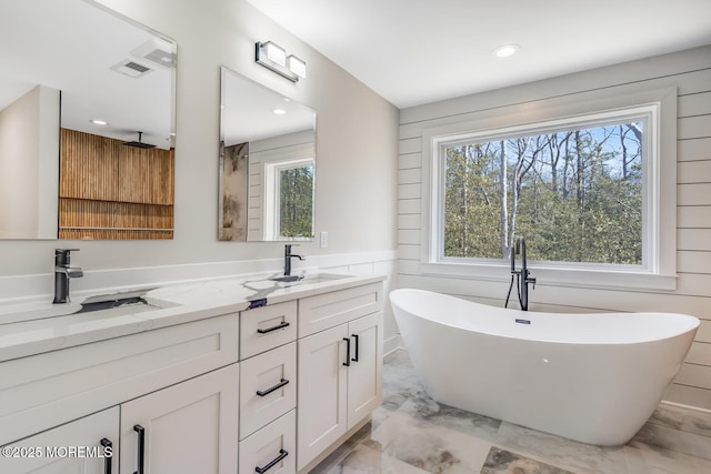 full bathroom with double vanity, marble finish floor, a freestanding bath, and a sink