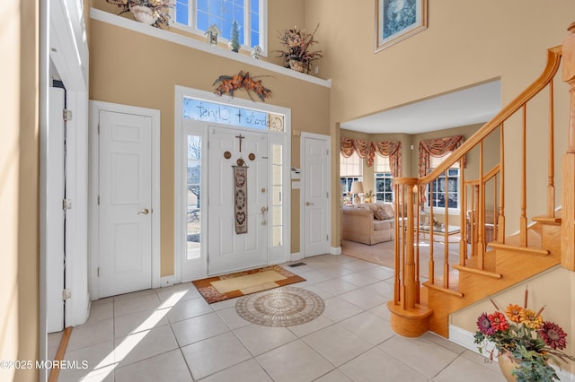 tiled entrance foyer with stairs, a high ceiling, and baseboards