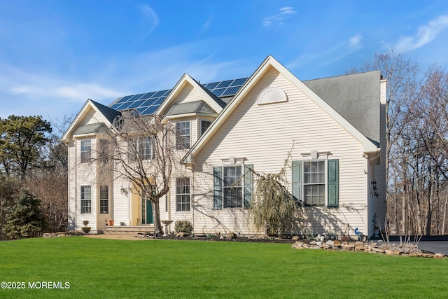 view of front of home featuring a shingled roof, roof mounted solar panels, a chimney, and a front lawn