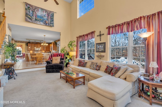 living area featuring ceiling fan with notable chandelier, carpet flooring, and a towering ceiling