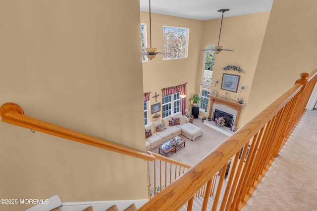 stairway with ceiling fan, a high ceiling, carpet, and a high end fireplace