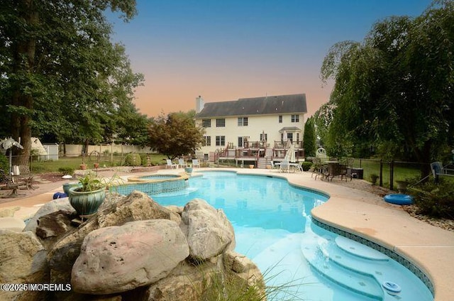 pool at dusk featuring a pool with connected hot tub, fence, and a patio