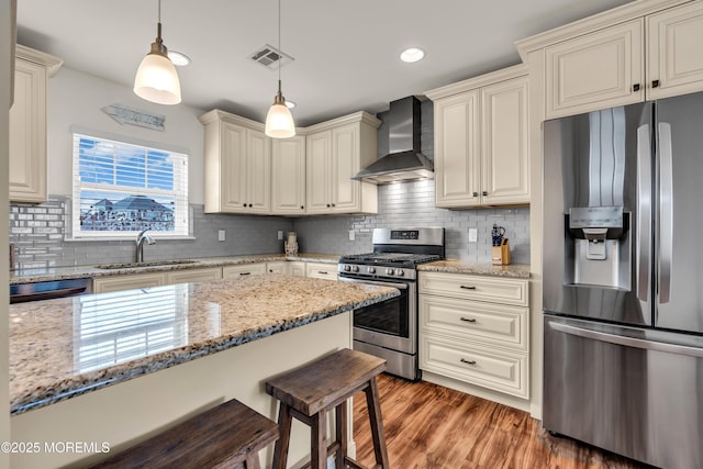 kitchen featuring visible vents, light wood-style flooring, a sink, appliances with stainless steel finishes, and wall chimney range hood