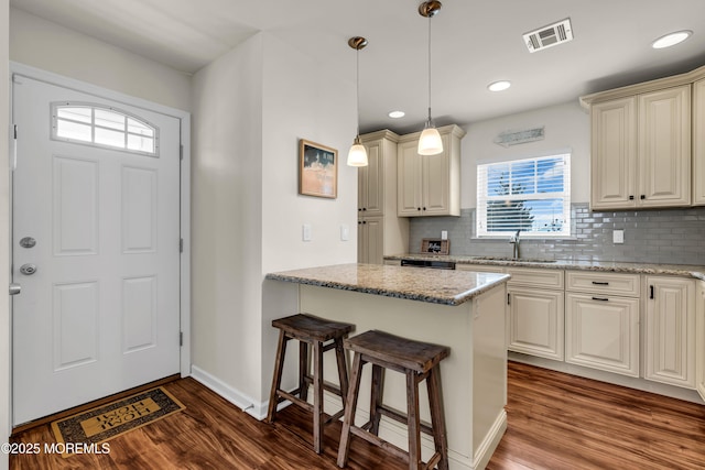 kitchen featuring dark wood-style floors, visible vents, a kitchen breakfast bar, and decorative backsplash