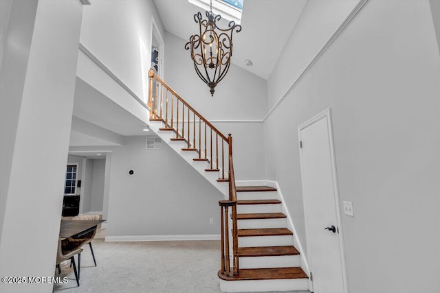 staircase with a notable chandelier, baseboards, visible vents, and a towering ceiling