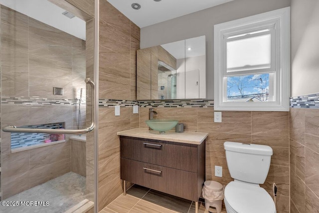 full bathroom featuring vanity, visible vents, a tile shower, tile walls, and toilet