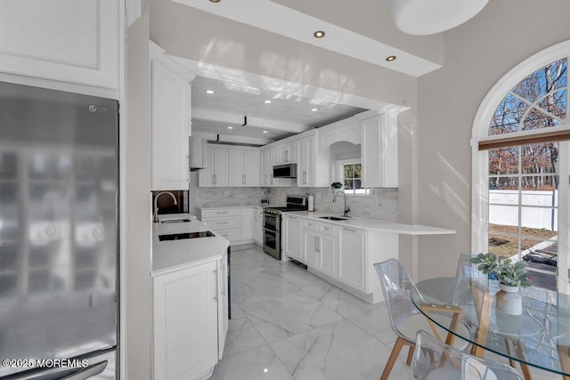 kitchen with marble finish floor, a sink, backsplash, white cabinetry, and appliances with stainless steel finishes