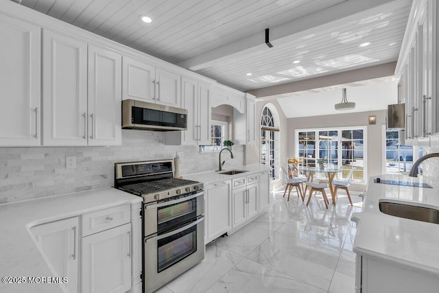 kitchen with a sink, decorative backsplash, light countertops, white cabinets, and appliances with stainless steel finishes