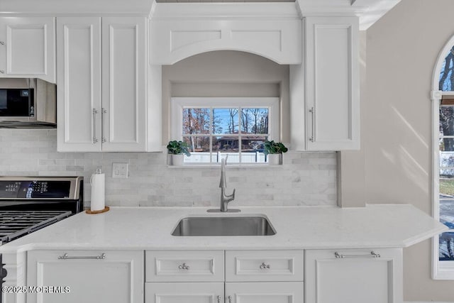 kitchen featuring tasteful backsplash, light stone countertops, appliances with stainless steel finishes, white cabinetry, and a sink