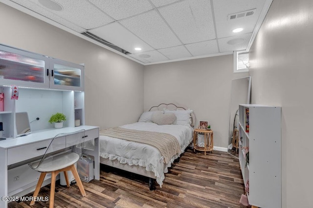 bedroom with visible vents, a drop ceiling, baseboards, and wood finished floors