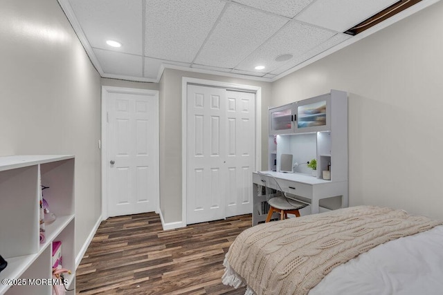 bedroom with a drop ceiling, dark wood finished floors, recessed lighting, a closet, and baseboards