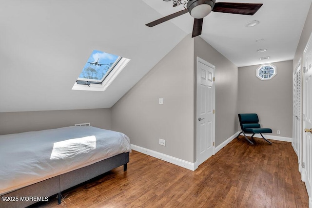 bedroom with baseboards, vaulted ceiling with skylight, wood finished floors, and a ceiling fan