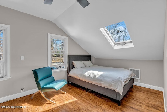 bedroom featuring lofted ceiling with skylight, visible vents, baseboards, and wood finished floors