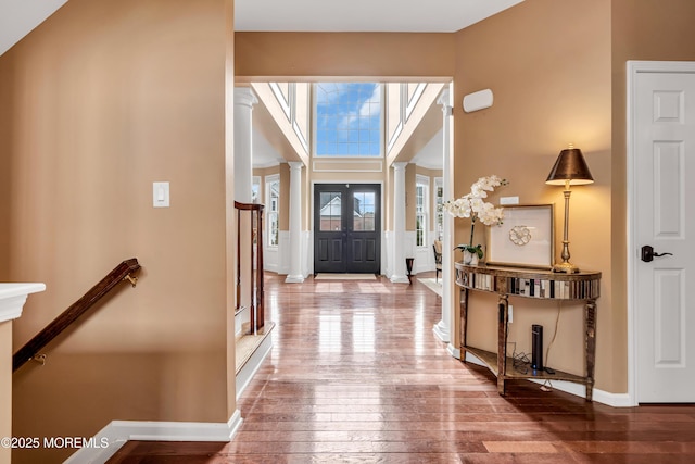 foyer with baseboards, a towering ceiling, hardwood / wood-style flooring, stairway, and ornate columns