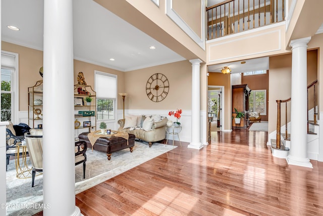 foyer featuring wood finished floors, stairs, ornamental molding, wainscoting, and ornate columns