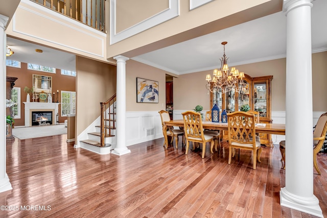 dining room with light wood-style floors, a glass covered fireplace, ornamental molding, stairs, and ornate columns