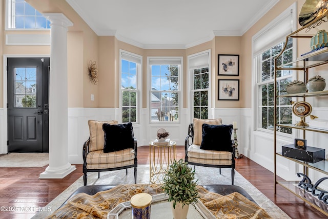 living area with a wainscoted wall, hardwood / wood-style floors, decorative columns, and crown molding