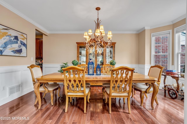 dining area featuring wainscoting, light wood-type flooring, visible vents, and crown molding