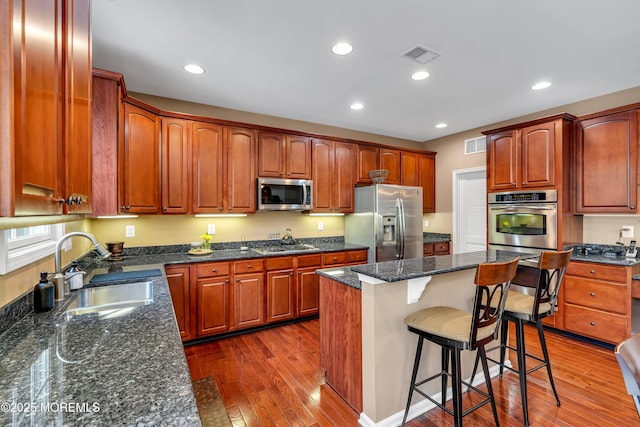 kitchen with stainless steel appliances, a breakfast bar, a sink, visible vents, and dark wood-style floors