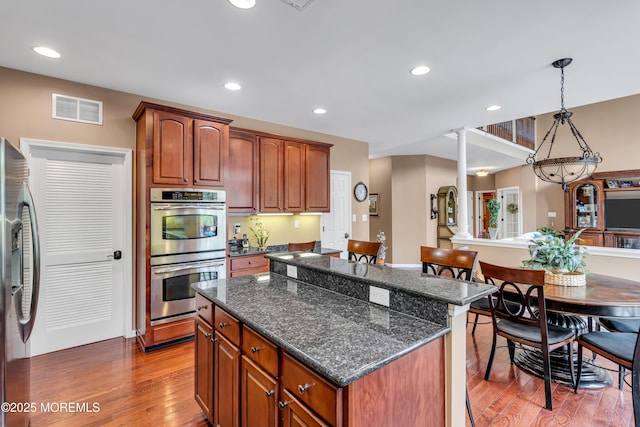 kitchen with visible vents, a center island, stainless steel appliances, light wood-type flooring, and ornate columns