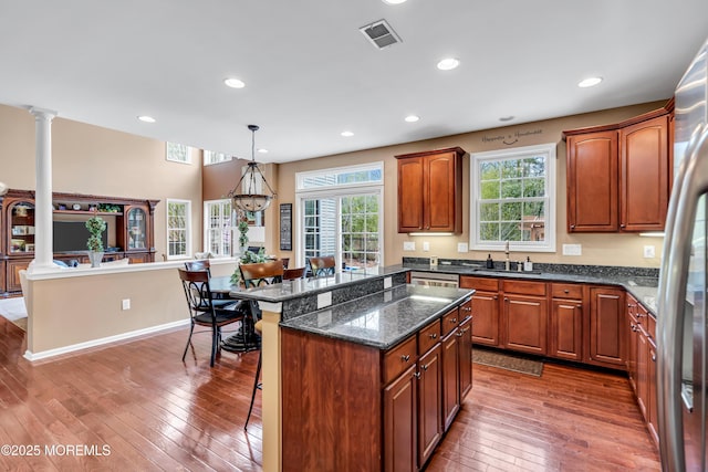 kitchen featuring decorative columns, visible vents, wood-type flooring, a kitchen breakfast bar, and a sink