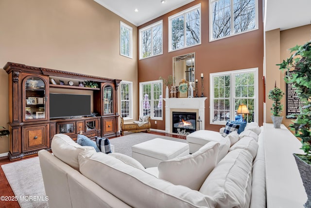 living area with a glass covered fireplace, recessed lighting, a high ceiling, and wood finished floors