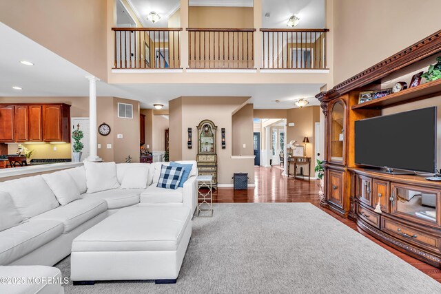 living area with wood finished floors, a towering ceiling, baseboards, visible vents, and ornate columns