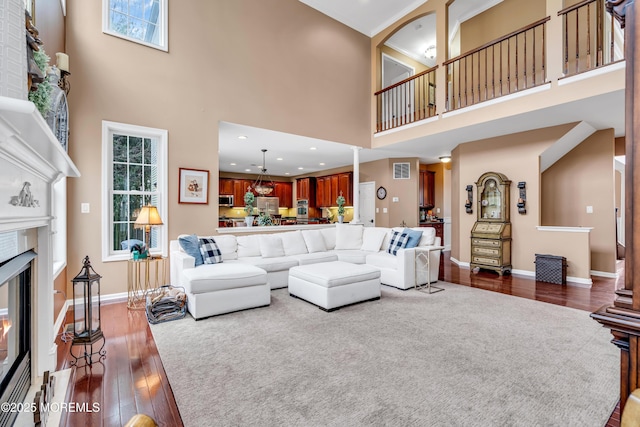 living area with visible vents, baseboards, a glass covered fireplace, dark wood-style flooring, and a high ceiling