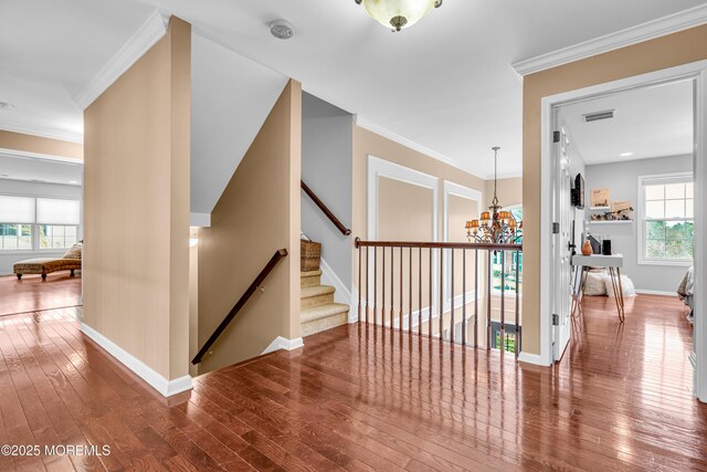 hallway with a notable chandelier, visible vents, baseboards, ornamental molding, and wood-type flooring