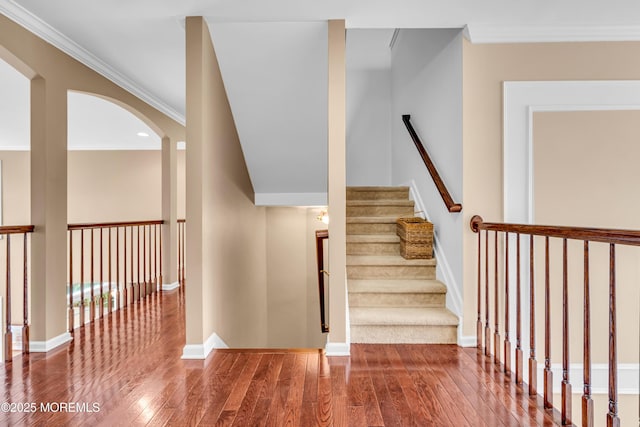 staircase with wood-type flooring, baseboards, arched walkways, and ornamental molding