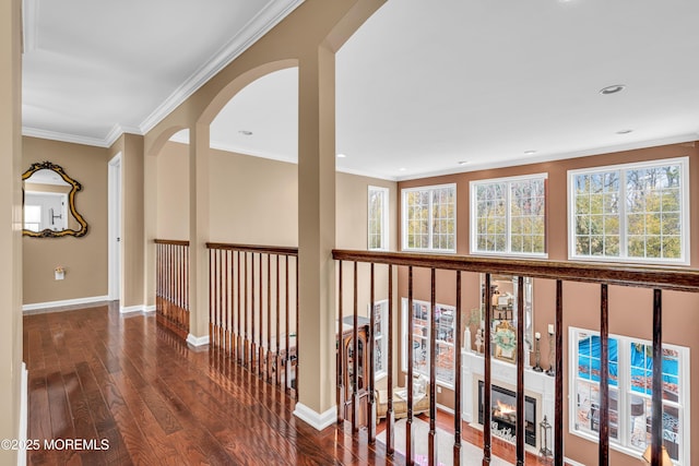 corridor featuring arched walkways, crown molding, baseboards, and hardwood / wood-style flooring