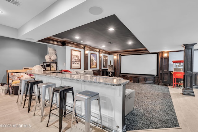 home theater with crown molding, recessed lighting, visible vents, a decorative wall, and light wood-style flooring