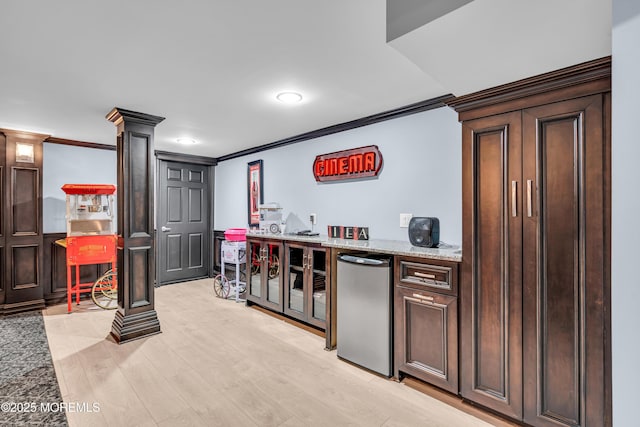 bar featuring ornate columns, light wood-style floors, crown molding, and refrigerator