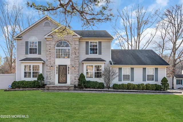 traditional home featuring brick siding, roof with shingles, fence, and a front yard