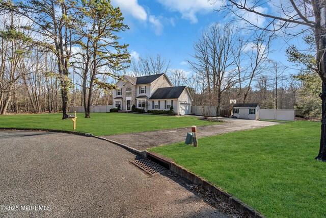 view of front facade with driveway, fence, a front lawn, and an outbuilding