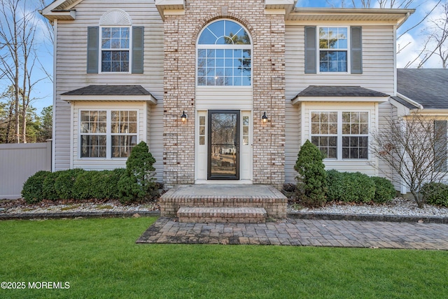 view of front of property featuring a front lawn, a shingled roof, fence, and brick siding