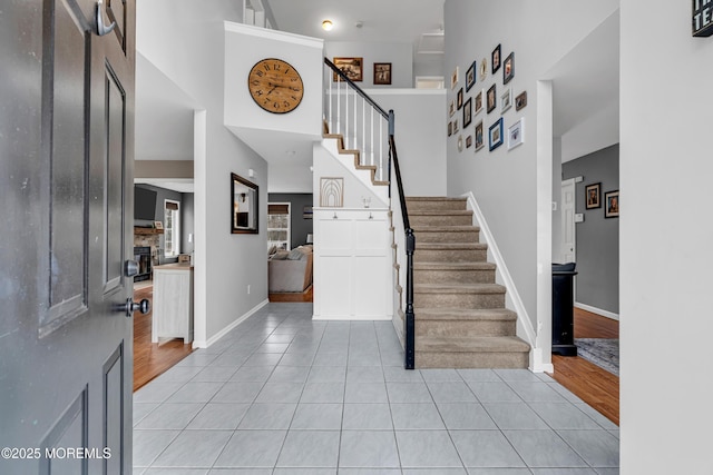 entryway with a towering ceiling, light tile patterned floors, baseboards, and stairway