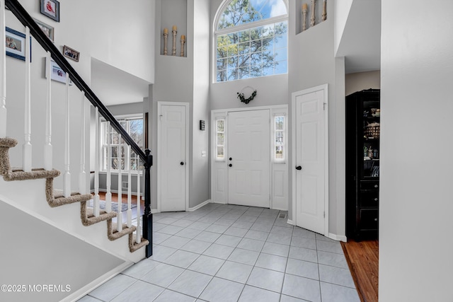 foyer entrance featuring a towering ceiling, baseboards, stairway, and light tile patterned flooring