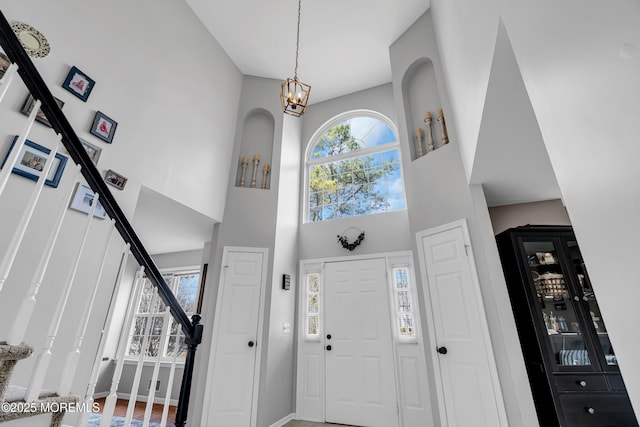 foyer entrance featuring a notable chandelier, a towering ceiling, baseboards, and stairs