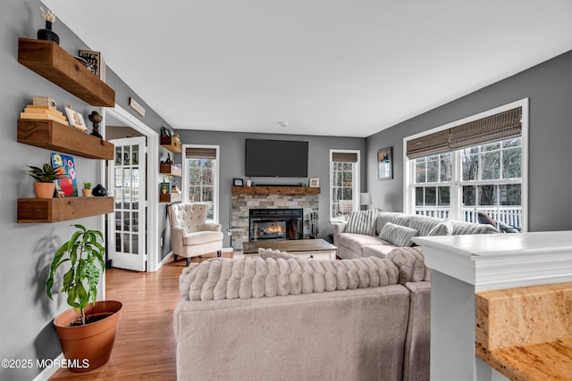 living area with plenty of natural light, baseboards, wood finished floors, and a stone fireplace