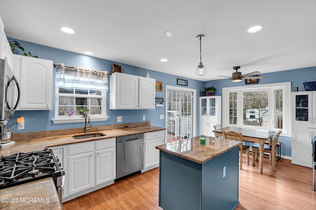 kitchen with light wood finished floors, appliances with stainless steel finishes, white cabinets, and a sink