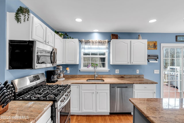 kitchen with light wood-style flooring, appliances with stainless steel finishes, a sink, white cabinetry, and a wealth of natural light