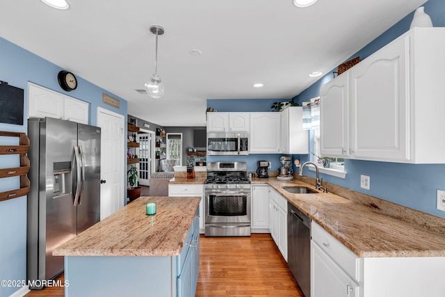 kitchen featuring light stone counters, appliances with stainless steel finishes, white cabinets, a sink, and a kitchen island