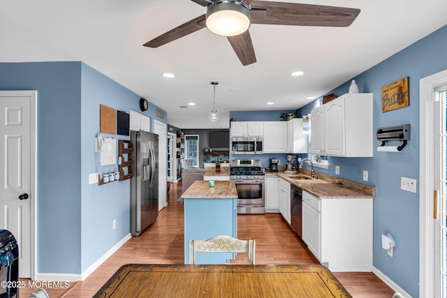 kitchen with light wood-style flooring, stainless steel appliances, a sink, white cabinetry, and a center island