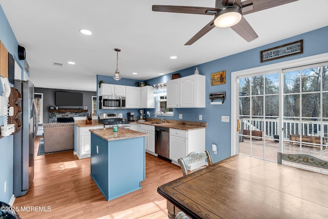 kitchen featuring stainless steel appliances, white cabinets, a sink, a kitchen island, and light wood-type flooring