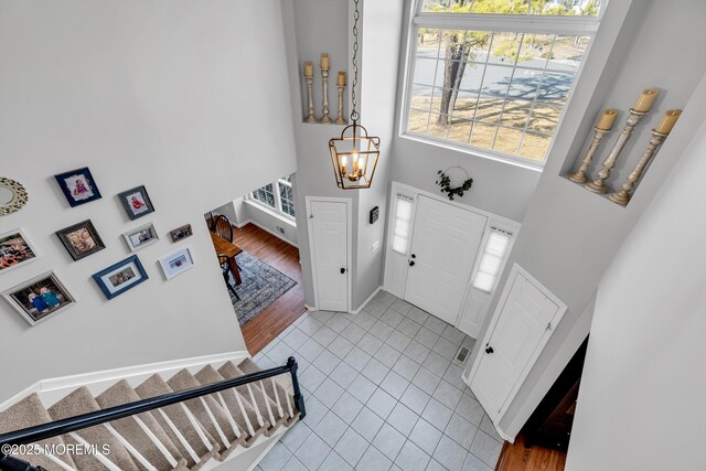 entryway featuring a chandelier, light tile patterned floors, a towering ceiling, baseboards, and stairway