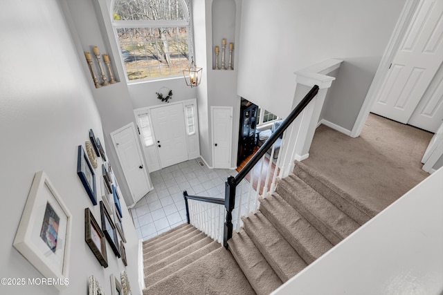 tiled foyer entrance featuring stairway, a towering ceiling, and baseboards