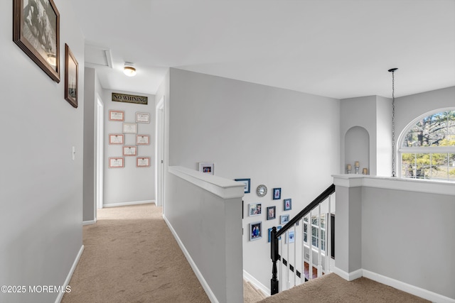 hallway with carpet floors, baseboards, and an upstairs landing