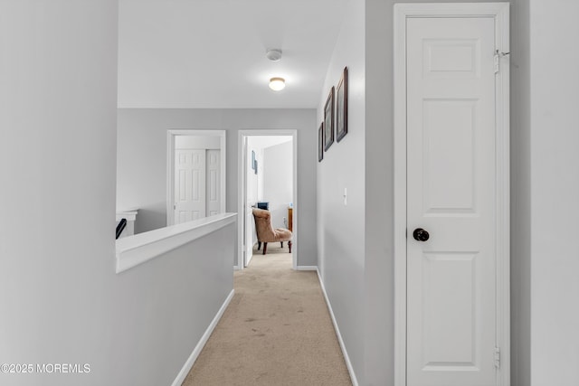 hall featuring baseboards, light carpet, and an upstairs landing